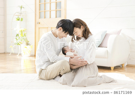 Portrait of a young mom, dad and three babies sitting in the living room and smiling Portrait of a young mom, dad and three babies sitting in the living room and smiling 86171169