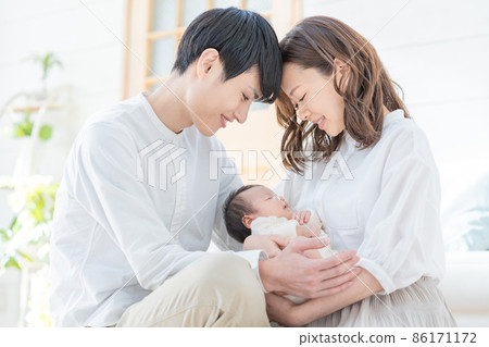 Portrait of a young mom, dad and three babies sitting in the living room and smiling Portrait of a young mom, dad and three babies sitting in the living room and smiling 86171172
