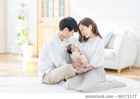 一位年輕媽媽、爸爸和三個嬰兒坐在客廳裡微笑的畫像 86171177