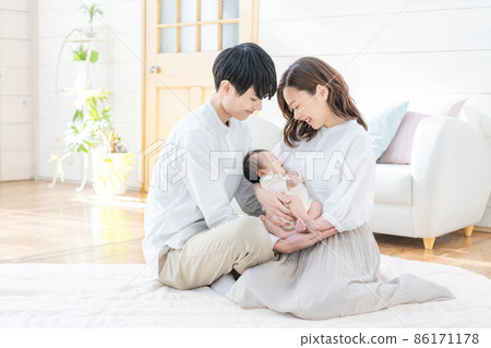 Portrait of a young mom, dad and three babies sitting in the living room and smiling 86171178