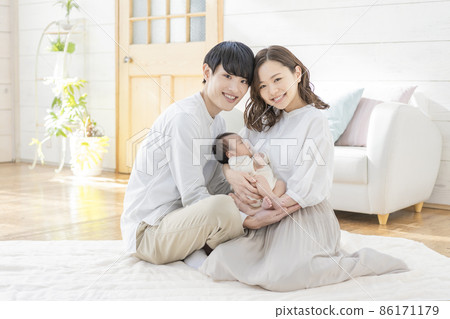 一位年輕媽媽、爸爸和三個嬰兒坐在客廳裡微笑的畫像 86171179