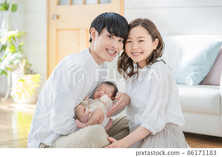Portrait of a young mom, dad and three babies sitting in the living room and smiling Portrait of a young mom, dad and three babies sitting in the living room and smiling 86171183