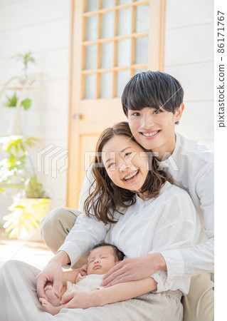 Portrait of a young mom, dad and three babies sitting in the living room and smiling Portrait of a young mom, dad and three babies sitting in the living room and smiling 86171767