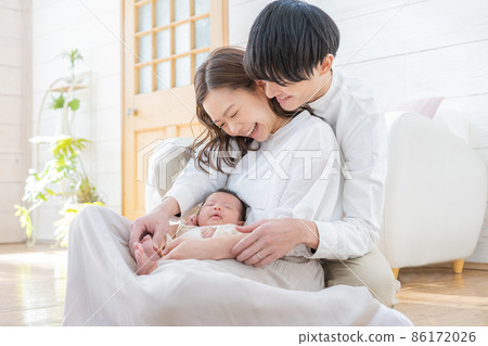 Portrait of a young mom, dad and three babies sitting in the living room and smiling 86172026