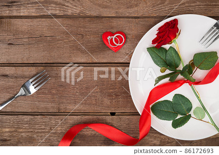 Valentine's Day dinner table setting with red ribbon, rose, knife and fork ring over oak background. Valentine's Day dinner table setting with red ribbon, rose, knife and fork ring over oak background. 86172693