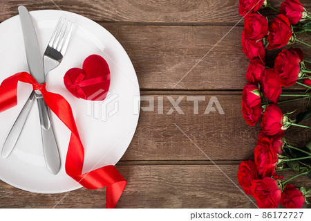 Valentines day table setting with plate, fork, knife, red heart, ribbon and roses. background Valentines day table setting with plate, fork, knife, red heart, ribbon and roses. background 86172727