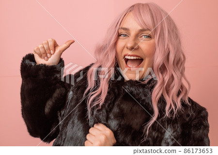 Happy and positive caucasian woman with pink curly hair wears black winter fur coat enjoying free time isolated over pink background. Happiness concept 86173653