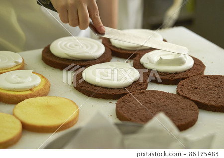 Confectionery image: Hands of a male pastry chef who applies cream to a sponge cake Confectionery image: Hands of a male pastry chef who applies cream to a sponge cake 86175483
