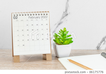 February 2022 desk calendar with plant on wooden table. 86175776