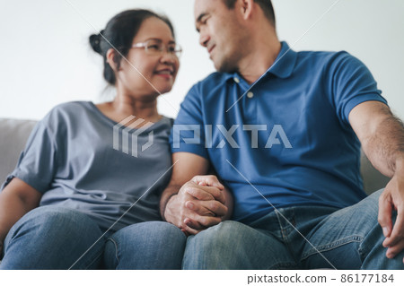 Portrait of Asian mature couple sitting in the living room. wife and husband hugging, holding hand with happiness and cheerful. Love, safety, and insurance family concept. 86177184