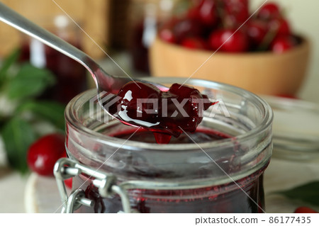 Glass jar and spoon with cherry jam, close up 86177435