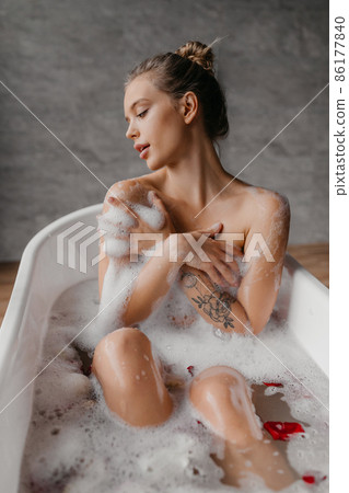 Skin care, clean body, spa treatments. Young lady in bathtub with petals, enjoying foam and hot water in bathroom Skin care, clean body, spa treatments. Young lady in bathtub with petals, enjoying foam and hot water in bathroom 86177840
