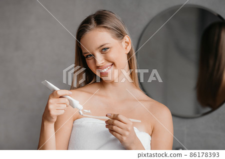 Daily dental care. Happy young lady pouring toothpaste on toothbrush, ready to clean her teeth in bathroom at home Daily dental care. Happy young lady pouring toothpaste on toothbrush, ready to clean her teeth in bathroom at home 86178393