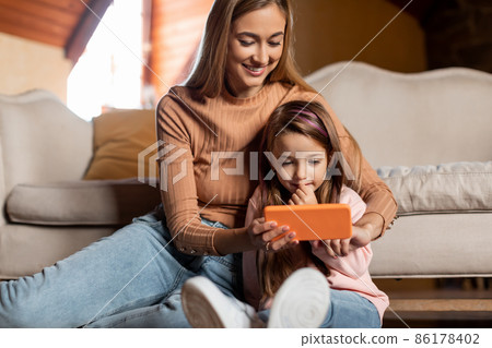 Portrait of smiling woman and girl using smartphone at home 86178402