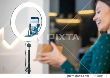 Young smiling beauty coach presenting new beauty products to online audience Young smiling beauty coach presenting new beauty products to online audience 86180595