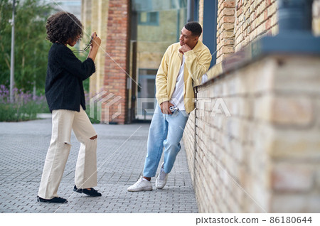 Woman taking picture of posing man sideways to camera Woman taking picture of posing man sideways to camera 86180644