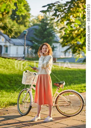 Girl in pinky skirt with a bike in the park Girl in pinky skirt with a bike in the park 86180733
