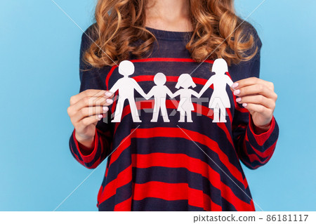Unknown woman wearing striped casual style sweater, woman holding paper family chain, relationships between children and parents. Indoor studio shot isolated on blue background. Unknown woman wearing striped casual style sweater, woman holding paper family chain, relationships between children and parents. Indoor studio shot isolated on blue background. 86181117