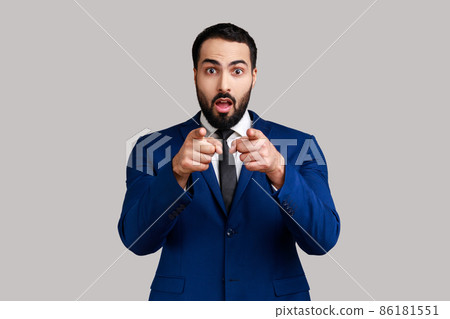 Astonished bearded man pointing to camera, standing with surprised shocked expression on face, hard to believe, wearing official style suit. Indoor studio shot isolated on gray background. 86181551