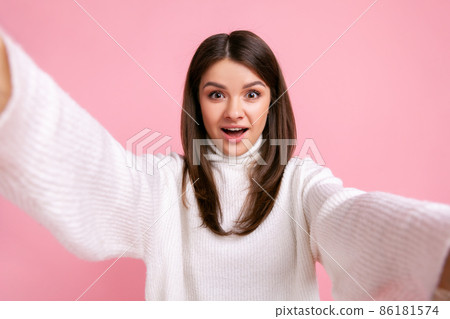 Excited brunette female makes point of view photo, looking with with big eyes, expressing excitement, wearing white casual style sweater. Indoor studio shot isolated on pink background. Excited brunette female makes point of view photo, looking with with big eyes, expressing excitement, wearing white casual style sweater. Indoor studio shot isolated on pink background. 86181574