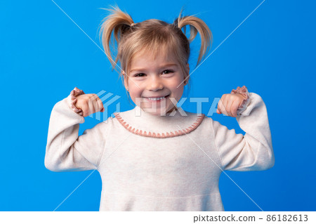 Little cute girl showing her strength against blue background Little cute girl showing her strength against blue background 86182613