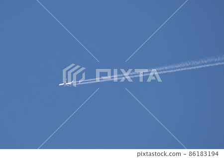 Distant passenger jet plane flying on high altitude on clear blue sky leaving white smoke trace of contrail behind. Air transportation concept 86183194
