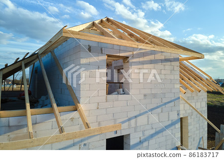 Aerial view of unfinished frame of private house with aerated lightweight concrete walls and wooden roof frame under construction. Aerial view of unfinished frame of private house with aerated lightweight concrete walls and wooden roof frame under construction. 86183717