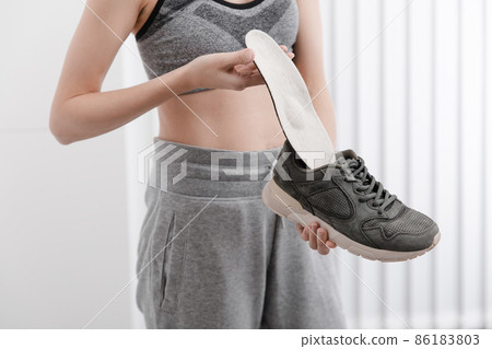 Woman putting orthopedic insole into shoe at home. Sports girl fitting orthopedic insole indoors, close up. Foot care banner. Flat Feet Correction. Treatment and prevention of foot diseases. Woman putting orthopedic insole into shoe at home. Sports girl fitting orthopedic insole indoors, close up. Foot care banner. Flat Feet Correction. Treatment and prevention of foot diseases. 86183803