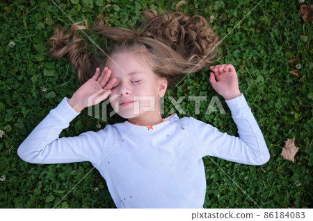 Portrait of pretty child girl outdoors lying down on grass lawn Portrait of pretty child girl outdoors lying down on grass lawn 86184083