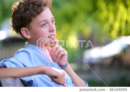 Young happy child boy relaxing sitting on bench in summer park. Positive kid enjoying summertime outdoors. Child wellbeing concept Young happy child boy relaxing sitting on bench in summer park. Positive kid enjoying summertime outdoors. Child wellbeing concept 86184089