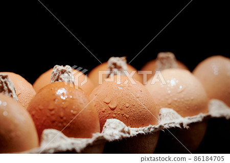 Wet eggs in a protective container on black background. Foreground and background in blur. 86184705
