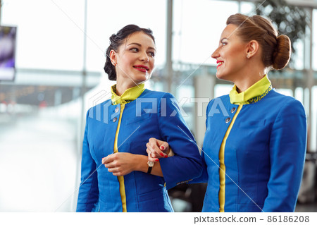 Two flight attendants walking arm in arm at airport terminal 86186208