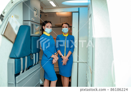 Flight attendants in medical masks standing in airplane cabin Flight attendants in medical masks standing in airplane cabin 86186224
