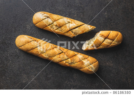 Roasted baguette with garlic butter. Crunchy sliced garlic bread on black table. 86186380