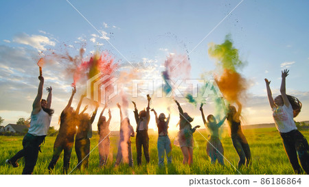 Cheerful girls toss up multi-colored powder at a beautiful sunset. 86186864