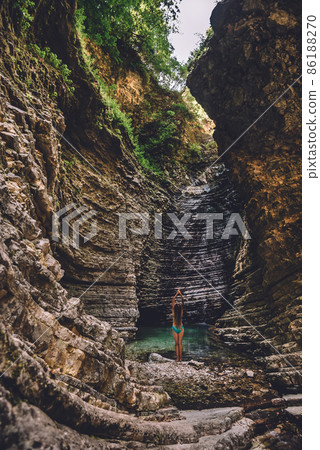 Girl in Swimsuit Standing at Waterfall Stretching Arms Girl in Swimsuit Standing at Waterfall Stretching Arms 86188270
