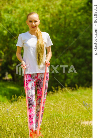 Girl doing exercises outdoor, using resistance fit band. 86188311
