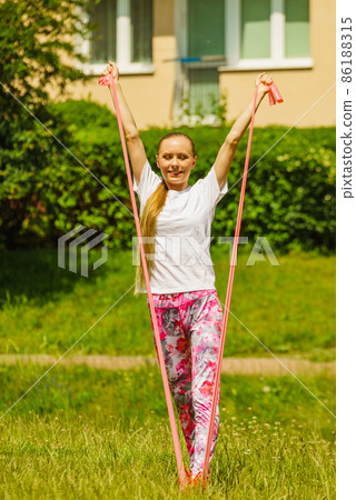 Girl doing exercises outdoor, using resistance fit band. 86188315