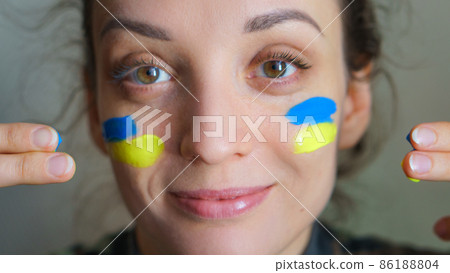 Indoor portrait of young girl with blue and yellow ukrainian flag on her cheek wearing military uniform, mandatory conscription in Ukraine, equality concepts 86188804