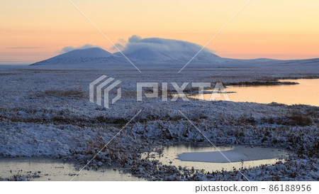 View of the snow-covered tundra, lakeside and snow-capped mountains at sunset 86188956