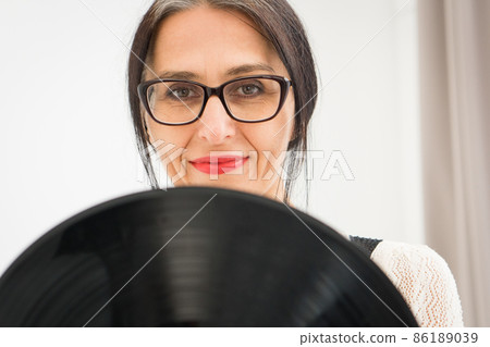 Studio photo of middle aged woman starting getting grey-haired wearing black and white clothes with vinyl record in hands on white background, middle age sexy lady, happy life concept Studio photo of middle aged woman starting getting grey-haired wearing black and white clothes with vinyl record in hands on white background, middle age sexy lady, happy life concept 86189039