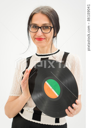 Studio photo of middle aged woman starting getting grey-haired wearing black and white clothes with vinyl record in hands on white background, middle age sexy lady, happy life concept Studio photo of middle aged woman starting getting grey-haired wearing black and white clothes with vinyl record in hands on white background, middle age sexy lady, happy life concept 86189041