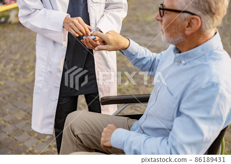 Doctor examining handicapped male patient in wheelchair with fingertip pulse oximeter outdoors 86189431