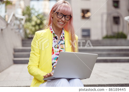 Joyful woman staring at computer screen on outdoor stairs Joyful woman staring at computer screen on outdoor stairs 86189445