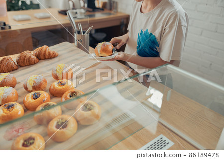 Young woman placing delicious bun on plate 86189478