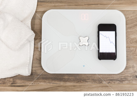 Smart scale standing on a floor connected to smartphone 86193223