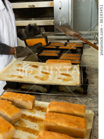 Baker hands with potholder next to metal cookie sheet with bread in oven Baker hands with potholder next to metal cookie sheet with bread in oven 86193451
