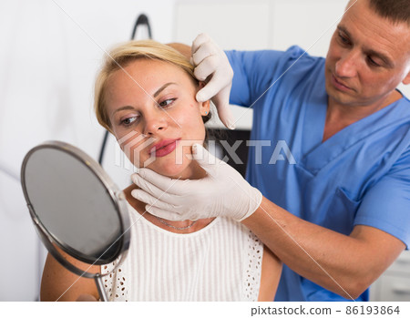 Specialist is analysing skin of female patient with using mirror before the procedure Specialist is analysing skin of female patient with using mirror before the procedure 86193864