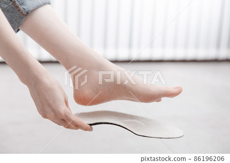Woman fitting orthopedic insole indoors, close up. Girl holding an insole next to foot at home. Orthopedic insoles. Foot care banner. Flat Feet Correction. Treatment and prevention of foot diseases. Woman fitting orthopedic insole indoors, close up. Girl holding an insole next to foot at home. Orthopedic insoles. Foot care banner. Flat Feet Correction. Treatment and prevention of foot diseases. 86196206