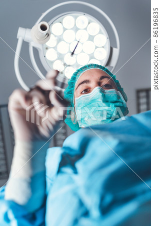 From below woman surgeon in medical uniform using professional tools while standing under bright From below woman surgeon in medical uniform using professional tools while standing under bright 86196835